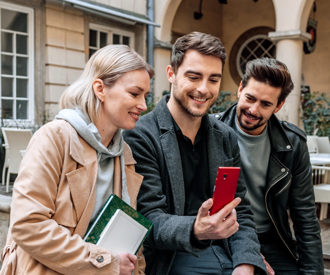 Three friends gathered around electronic translator, sharing a moment of excitement and curiosity as they look at the screen together. 